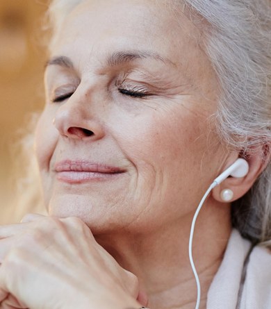 Una dona escolta música amb auriculars i els ulls tancats durant un exercici de relaxació.