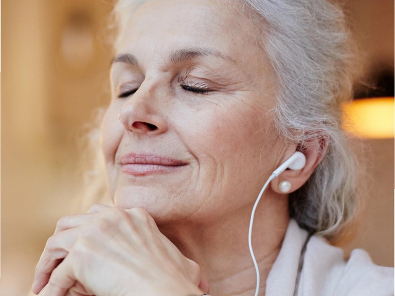Una dona escolta música amb auriculars i els ulls tancats durant un exercici de relaxació.